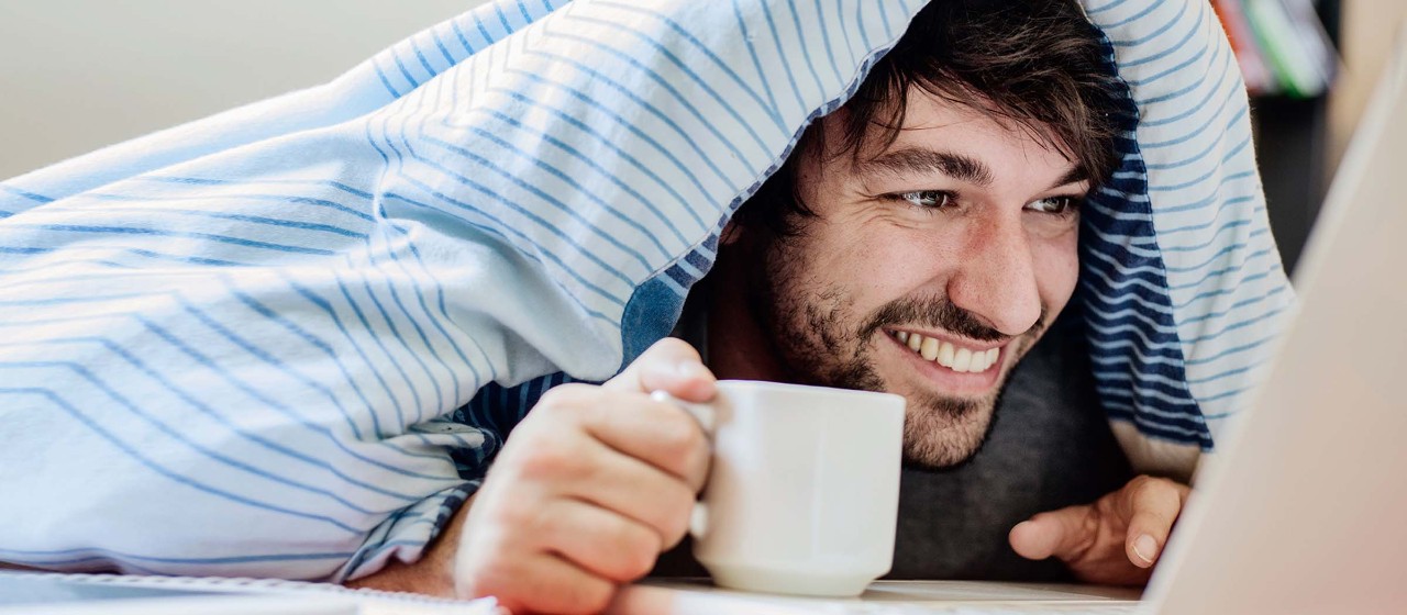 Mann mit einer Tasse Kaffee unter der Decke