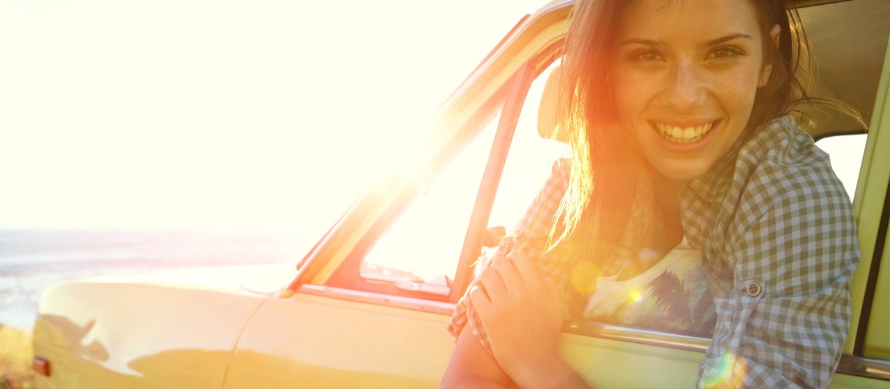 Frau die glücklich aus dem Auto schaut mit Sonnenuntergang.